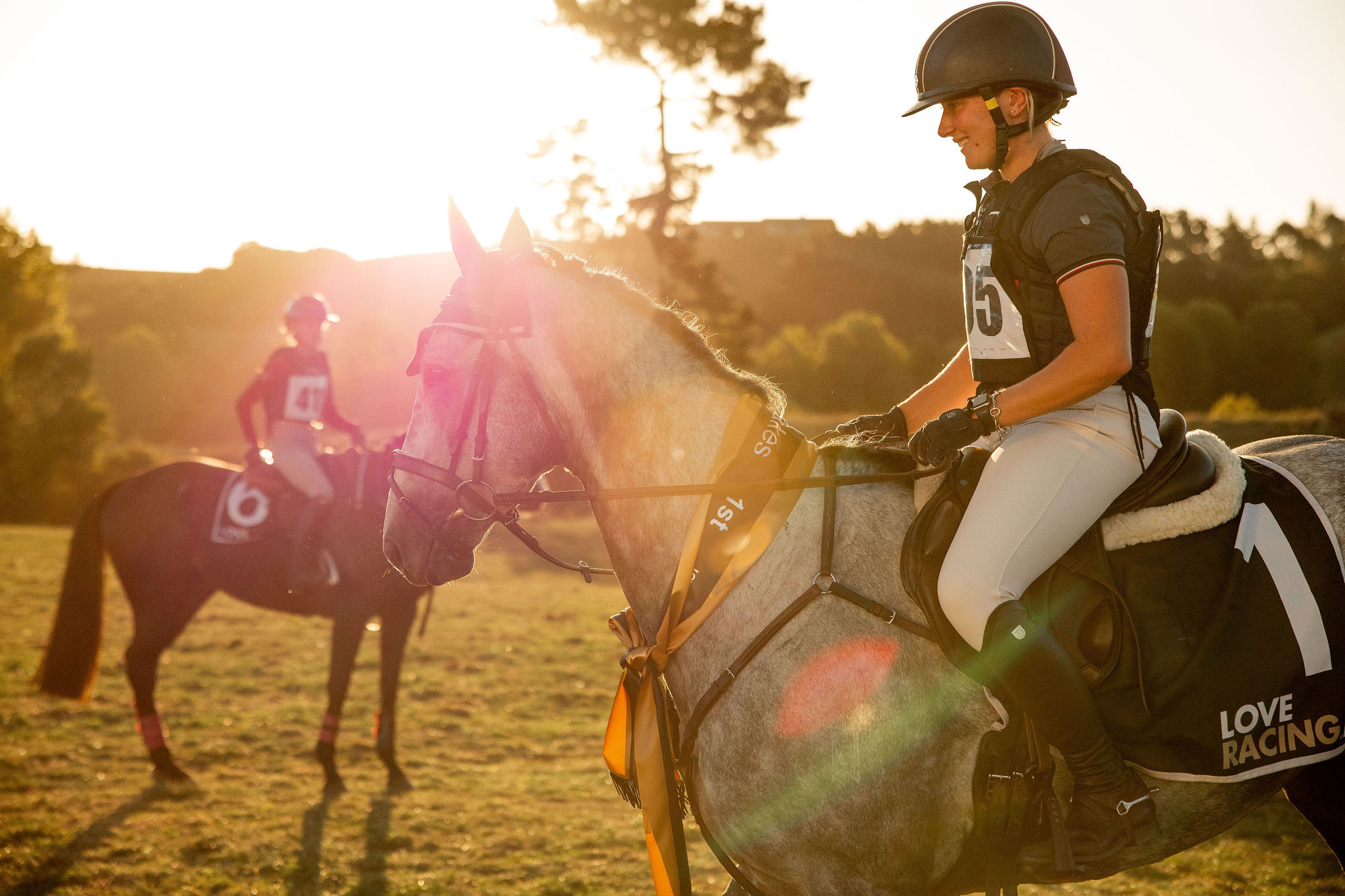 Equestrian rider on a horse at sunset, with another rider in the background.