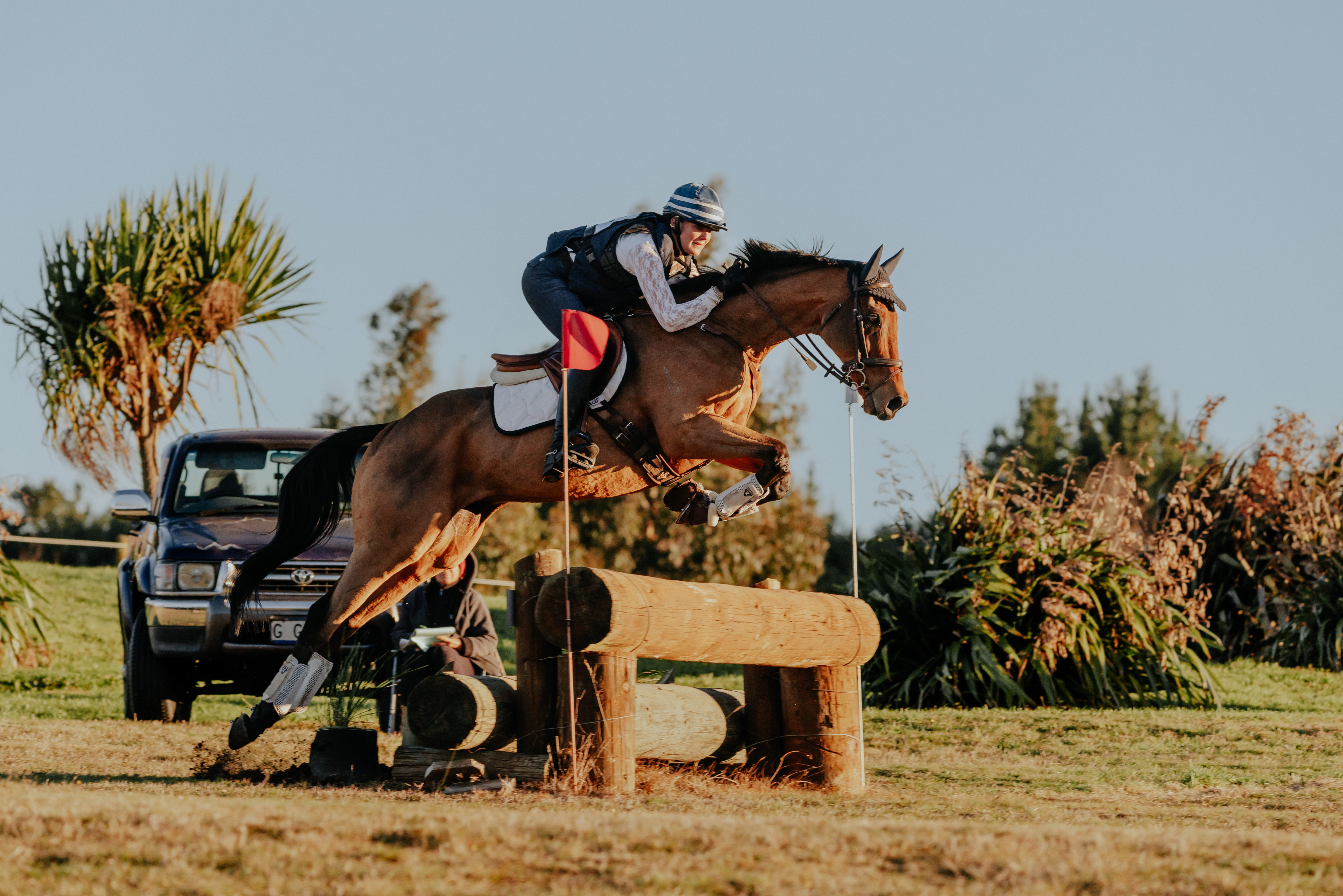 Equestrian rider jumping a brown horse over a wooden obstacle outdoors