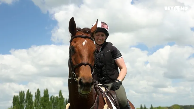 Smiling rider on a brown horse under a cloudy blue sky