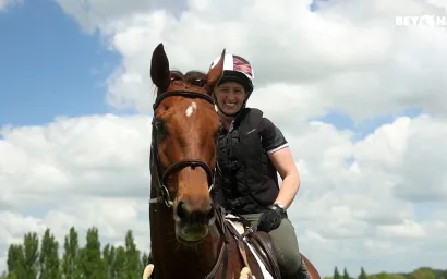 Smiling rider on a brown horse under a cloudy blue sky